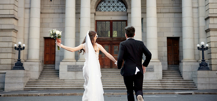 A bride and groom smile at each other entering building